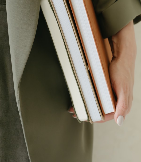 A stack of clinical training texts held close — preparation and accountability behind the work